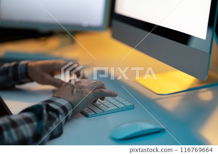 Man Typing on Keyboard in Dimly Lit Office Workspace 116769664