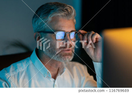 Mature Man Focusing on Computer Screen While Working Late at Night 116769689