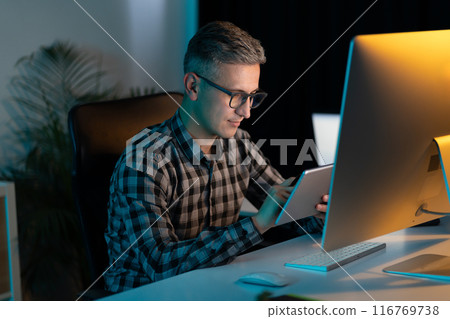 Man Working Late at Night on Digital Tablet in Office Man Working Late at Night on Digital Tablet in Office 116769738