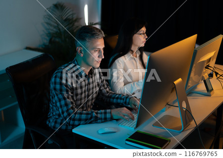 Focused Professionals Working Late on Computers in an Office 116769765