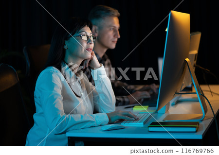 Two Professionals Working at Computers in Dark Office Setting Two Professionals Working at Computers in Dark Office Setting 116769766