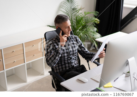 Businessman Talking on Phone and Reviewing Documents in Modern Office 116769867