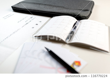 A handwritten meal order, a new schedule book, a farewell gift envelope and a brush pen are laid out on a white desk. 116770224