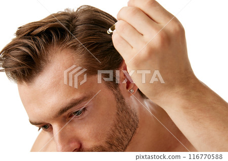 Modern male grooming and self-care routines. Handsome shirtless man taking care after hair, applying serum isolated on white background 116770588
