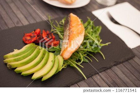 Baked sea trout fillet with fresh vegetables and herbs on black board Baked sea trout fillet with fresh vegetables and herbs on black board 116771541