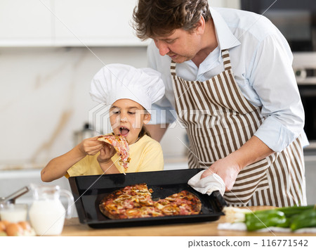 Daughter eats pizza prepared by father Daughter eats pizza prepared by father 116771542