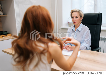 View from shoulder of unrecognizable woman patient to skilled middle-aged female doctor explaining medical report results or news about rehabilitation, speaking helping advice. Concept of healthcare. 116771709