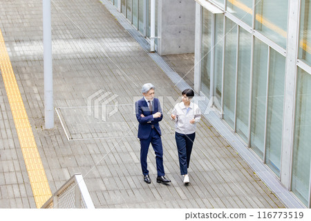 A businessman and an engineer walking down an aisle while talking A businessman and an engineer walking down an aisle while talking 116773519