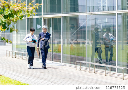 A businessman and an engineer having a conversation while walking outside the facility A businessman and an engineer having a conversation while walking outside the facility 116773525
