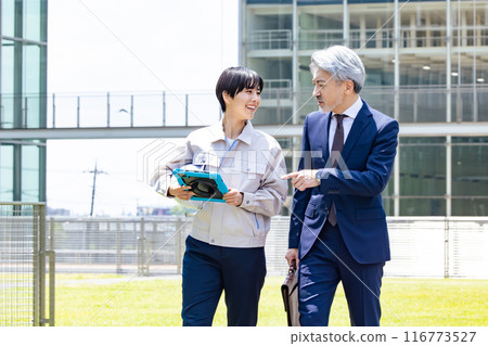 A businessman and an engineer having a conversation while walking outside the facility 116773527