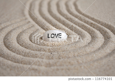Love text engraved on Zen stone on sand with shining light. Love and romance concept 116774101