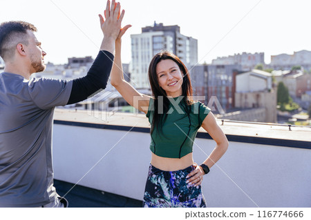 Handsome husband and wife enjoying end of physical morning warm-up. Two athletic people greeting each other with high five gesture during fit training on rooftop. Handsome husband and wife enjoying end of physical morning warm-up. Two athletic people greeting each other with high five gesture during fit training on rooftop. 116774666