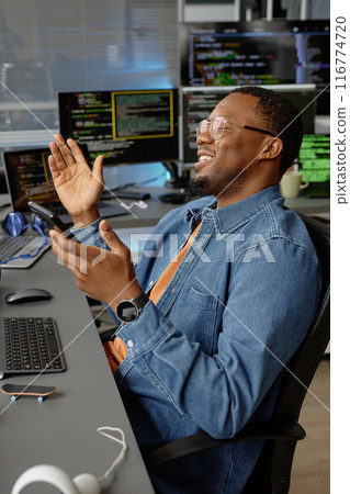 Vertical shot of happy male African American software developer at working desk with multiple screens rejoicing at fixing error celebrating success at office, copy space Vertical shot of happy male African American software developer at working desk with multiple screens rejoicing at fixing error celebrating success at office, copy space 116774720