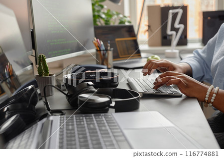 Close up on female hands typing on computer keyboard and headphones lying on working desk of software developer, office setup Close up on female hands typing on computer keyboard and headphones lying on working desk of software developer, office setup 116774881