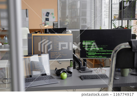 Background shot of programmer desk setup with laptop and computer screens displaying source code in empty software development agency office 116774917