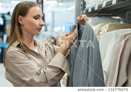 Young woman customer shopping at textile department and choosing bathrobe at home goods store. Home decor and comfort concept Young woman customer shopping at textile department and choosing bathrobe at home goods store. Home decor and comfort concept 116776078