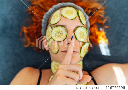 close-up face red-haired young woman with round slices of cucumber, cucumber mask on face 116776396