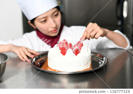 A female pastry chef preparing a whole cake A female pastry chef preparing a whole cake 116777329