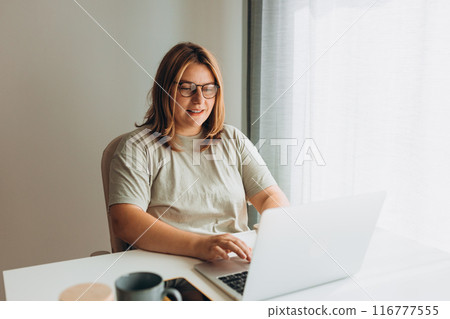 Happy cheerful cute beautiful business woman in glasses sit indoors in office using laptop computer. Positive creative woman checking content on web page via laptop computer sitting in coworking space Happy cheerful cute beautiful business woman in glasses sit indoors in office using laptop computer. Positive creative woman checking content on web page via laptop computer sitting in coworking space 116777555