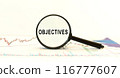 Magnifying Glass with text Objectives on on background with charts. Business Concept. Front view. Objectives word 116777607