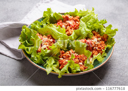 Lettuce wraps filled with minced meat and topped with peanuts and chili pepper flakes on a plate, healthy protein dish Lettuce wraps filled with minced meat and topped with peanuts and chili pepper flakes on a plate, healthy protein dish 116777618