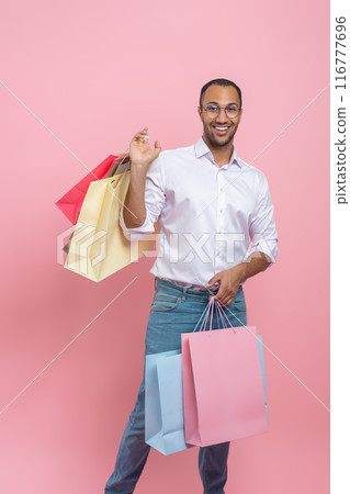 Cheerful African American man wearing shirt and glasses with paper bags enjoying shopping 116777696