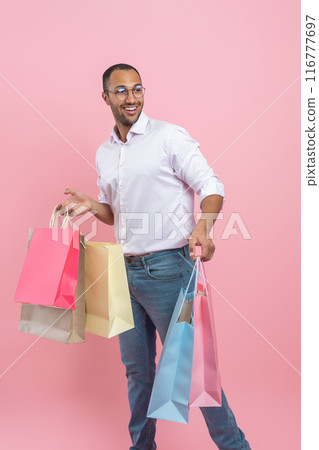 Smiling African American man wearing shirt and glasses holding shopping bags looking away Smiling African American man wearing shirt and glasses holding shopping bags looking away 116777697