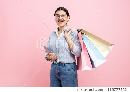 Excited woman wearing glasses shirt and jeans holding shopping bags and tablet enjoying online purchasing Excited woman wearing glasses shirt and jeans holding shopping bags and tablet enjoying online purchasing 116777732