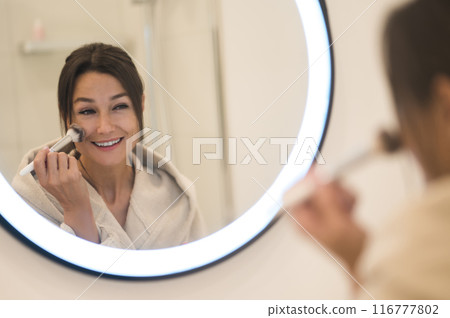 Cute caucasian dark-haired woman at the mirror in the bathroom Cute caucasian dark-haired woman at the mirror in the bathroom 116777802