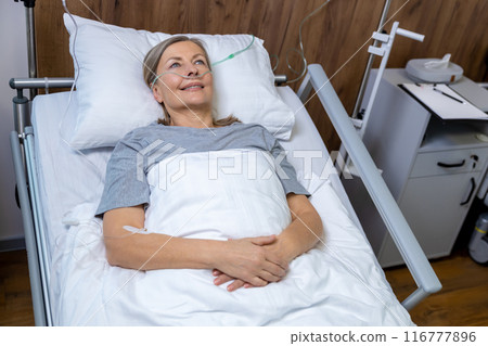 Mid aged woman lying in bed in an intensive therapy department Mid aged woman lying in bed in an intensive therapy department 116777896