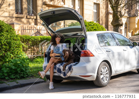 Young woman with dog sitting in the car with open car trunk 116777931
