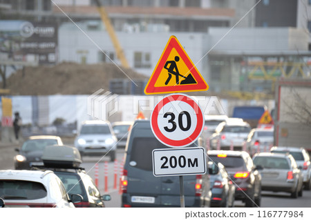 Roadworks warning traffic signs of construction work on city street and slowly moving cars 116777984