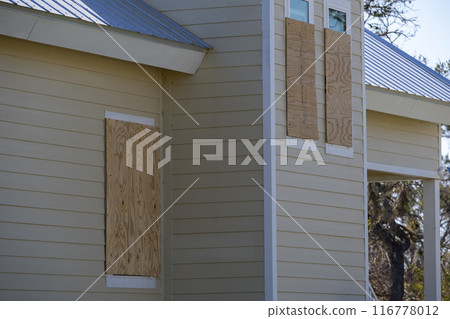 Plywood mounted as storm shutters for hurricane protection of house windows. Protective measures before natural disaster in Florida 116778012