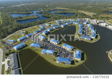 Hurricane damaged apartment buildings rooftops covered with protective plastic tarp against rain water leaking until replacement of asphalt shingles. Aftermath of natural disaster Hurricane damaged apartment buildings rooftops covered with protective plastic tarp against rain water leaking until replacement of asphalt shingles. Aftermath of natural disaster 116778102
