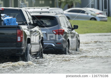 Hurricahe rainfall flooded Florida road with evacuating cars and surrounded with water houses in suburban residential area 116778106