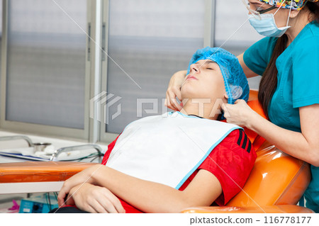 Young male patient being prepared for a skin lesion removal procedure. Dermatologist carrying out a removal of benign skin lesion on the face of a young male patient. 116778177
