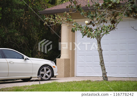 Vehicle parked in front of wide garage double door on paved driveway of typical contemporary american home Vehicle parked in front of wide garage double door on paved driveway of typical contemporary american home 116778242
