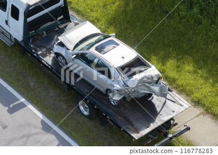 Tow truck hauling smashed vehicle on car accident site. Emergency services personnel responding to traffic crash on American street. First responders helping on road in the USA Tow truck hauling smashed vehicle on car accident site. Emergency services personnel responding to traffic crash on American street. First responders helping on road in the USA 116778283
