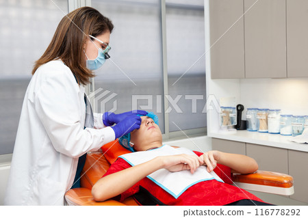 Skin lesion removal procedure. Dermatologist carrying out a removal of benign skin lesion on the face of a young male patient. 116778292