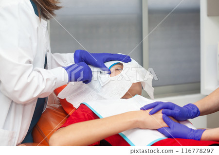 Skin lesion removal procedure. Dermatologist carrying out a removal of benign skin lesion on the face of a young male patient. 116778297
