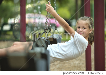 Young pretty smiling teenage girl playing alone on swings on summer playground 116778512