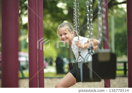 Young pretty happy smiling teenage small girl having fun on playground swings on summer vacations sunny day Young pretty happy smiling teenage small girl having fun on playground swings on summer vacations sunny day 116778514