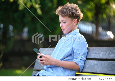 Young boy playing game on his smartphone outdoors in summer park. Addiction from electronic gadgets concept 116778536