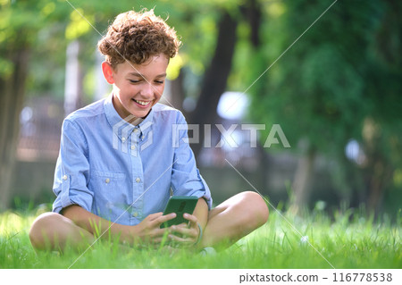 Young boy playing game on his smartphone outdoors in summer park. Addiction from electronic gadgets concept 116778538