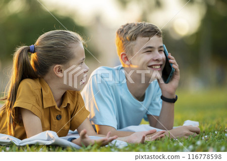 Sad teen friend being ignored by another outdoors while he is talking happily on mobile phone and paying no attention. Friendship problems concept Sad teen friend being ignored by another outdoors while he is talking happily on mobile phone and paying no attention. Friendship problems concept 116778598