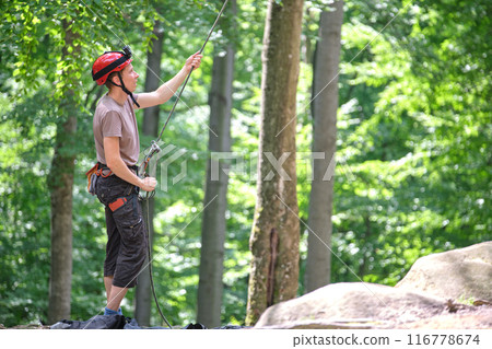 Man belays his partner climber with belaying device and rope. Climber's handsman holding equipment for rock mountaineering security. Man belays his partner climber with belaying device and rope. Climber's handsman holding equipment for rock mountaineering security. 116778674