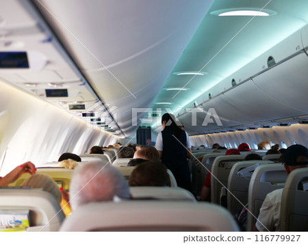 Passengers seated in plane cabin stewardesses in background. Ideal for aviation and travel videos. Plane interior view with people and crew, showcasing comfort and plane journey ambiance. Passengers seated in plane cabin stewardesses in background. Ideal for aviation and travel videos. Plane interior view with people and crew, showcasing comfort and plane journey ambiance. 116779927