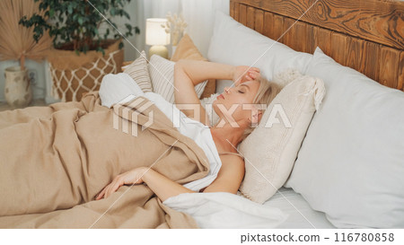 Leisure morning. Sleeping resting. Wonderful rest. Relaxed woman covered with blanket enjoying free time laying in comfortable bed in light home interior. 116780858