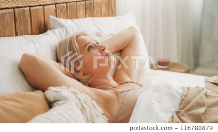 Depressing thoughts. Upset mood. Morning sadness. Confused sleepless woman feeling regret laying in bed covered with blanket in light interior bedroom at home. 116780879