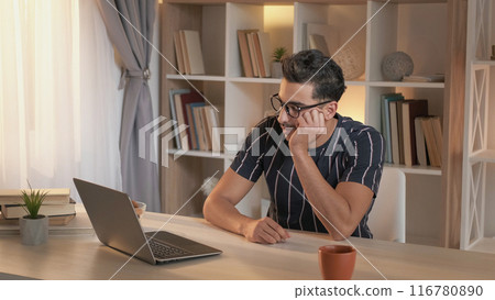 Boring video. Exhausted student. Online lesson. Tired man watching lecture on laptop falling asleep at desk sitting in modern light home interior. 116780890